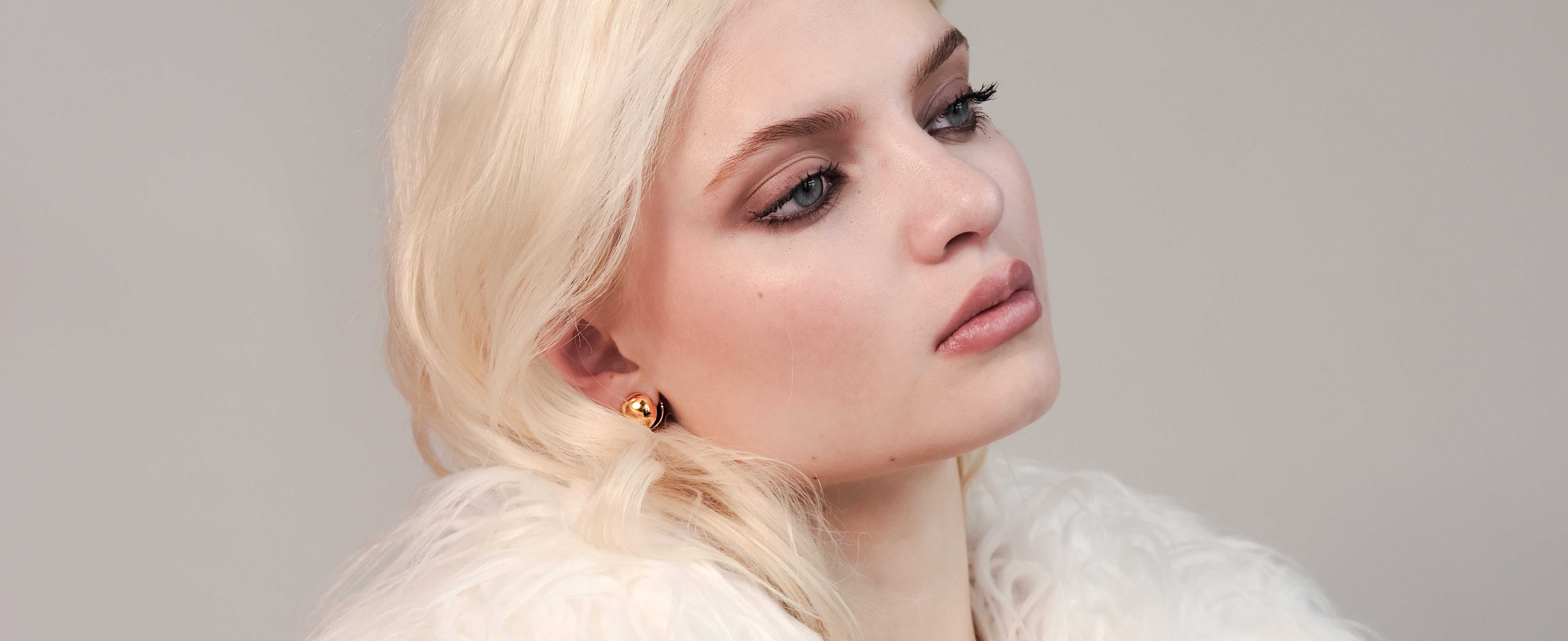 Orb Huggies worn by model, side-facing view highlighting the gold earrings' bold yet minimal 18k gold design and snug fit.