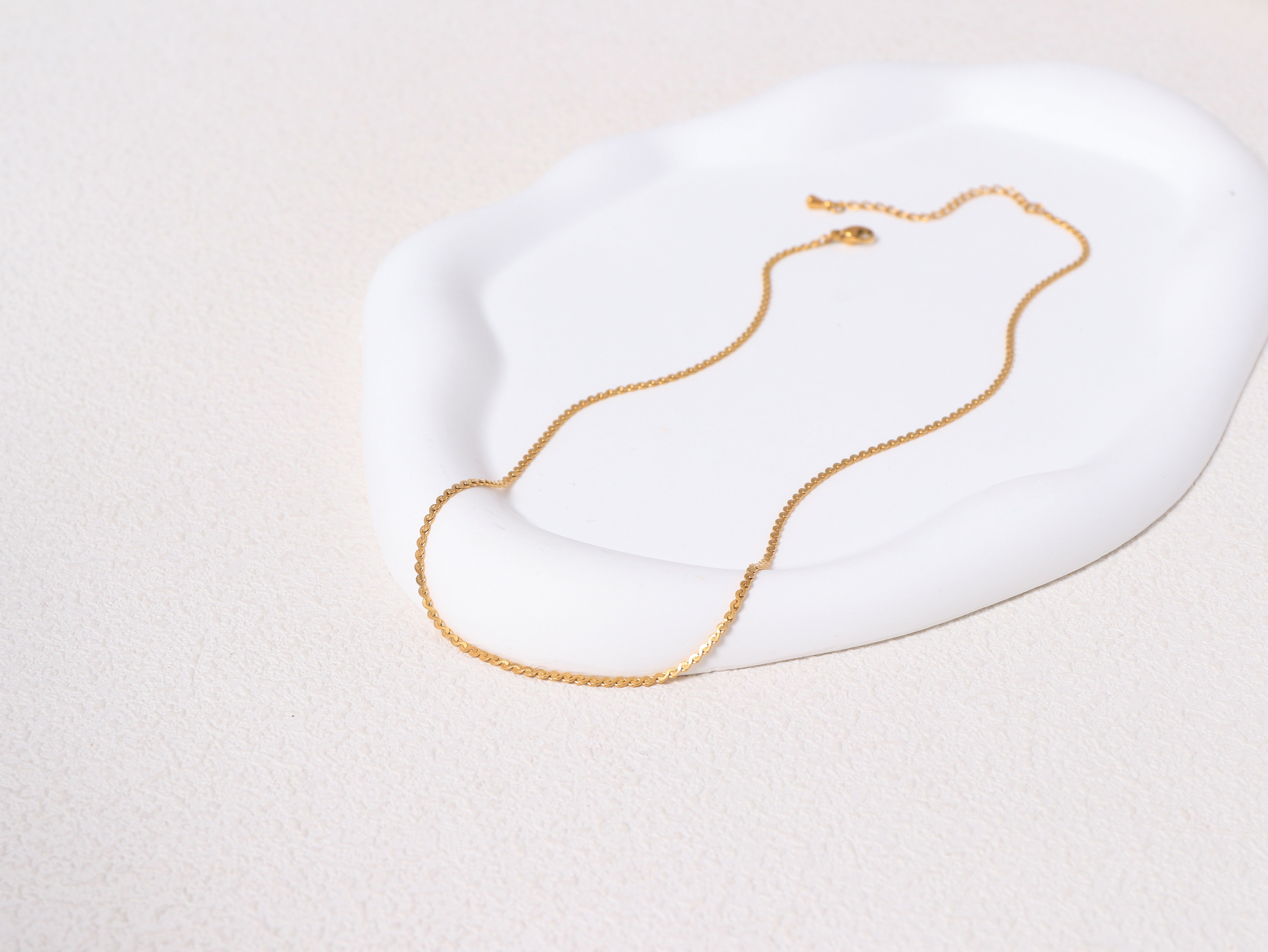 Allure Gold Chain resting on a neutral-toned jewelry base, showcasing the full length and minimalist 14k gold design.