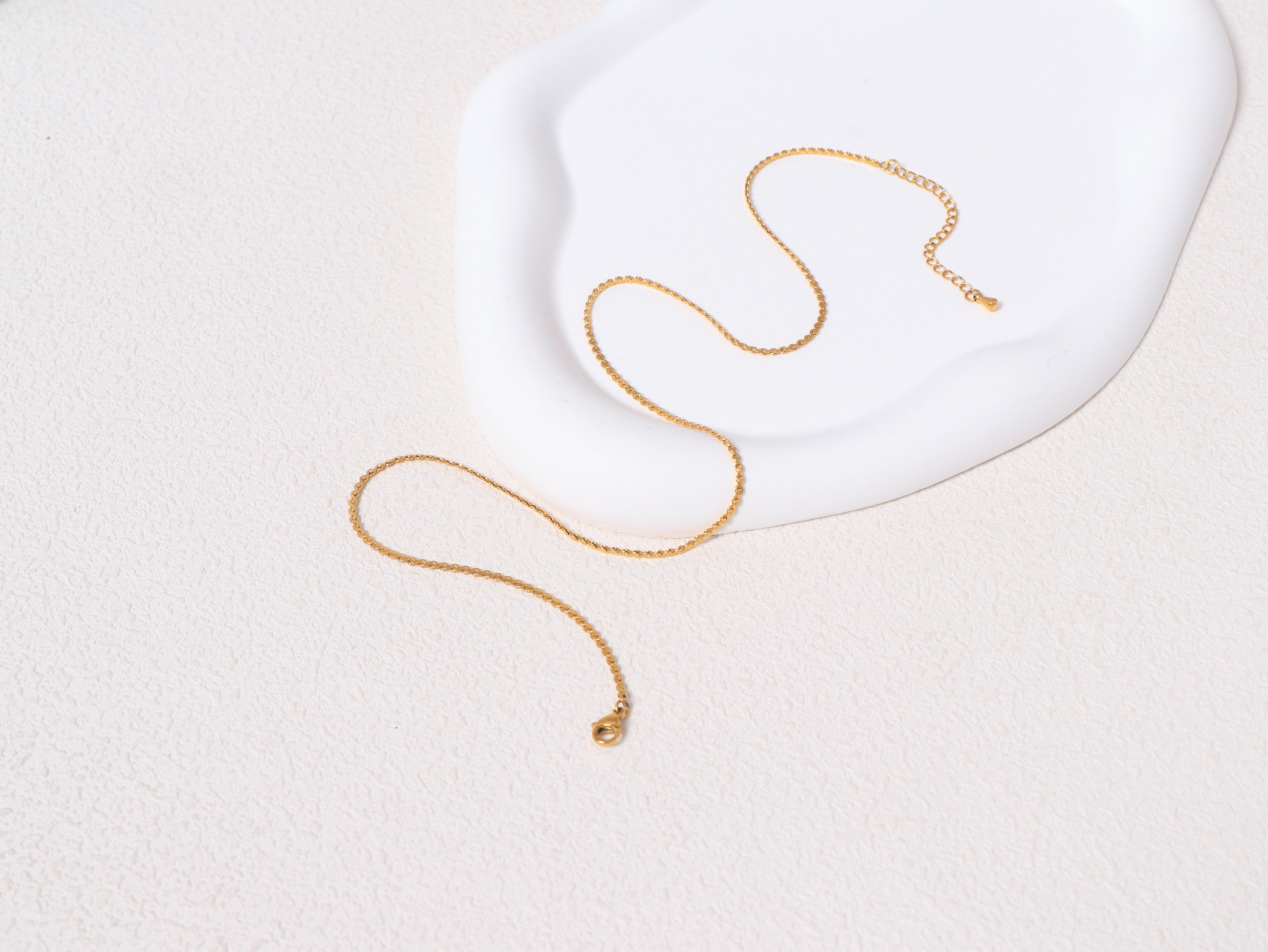 An opened Allure Gold Chain resting on a neutral-toned jewelry base, showcasing the full length and minimalist 14k gold design.