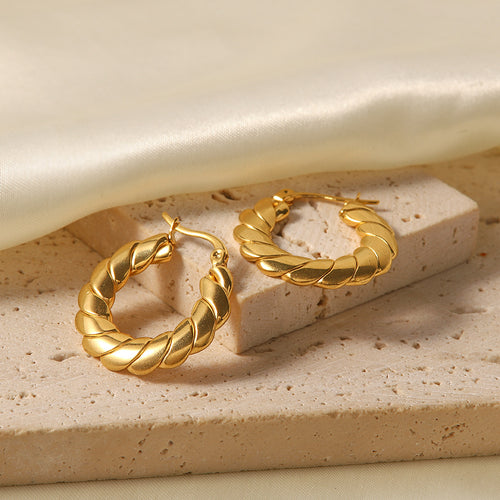 Styled flat lay of the Venus Gold Hoops, highlighting their design and radiant 18k gold tone against a soft, textured backdrop.