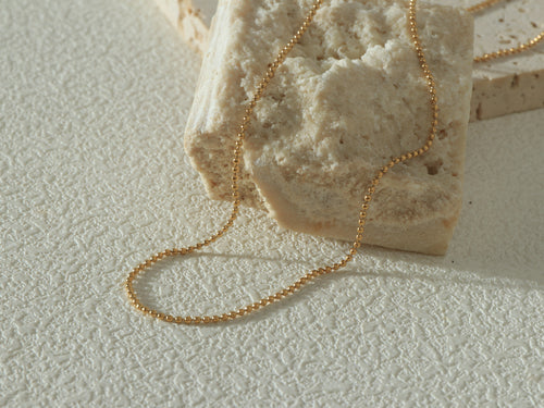 Grandeur Chain styled in a curved shape on a neutral background, showing its delicate profile and elegant gold tone.