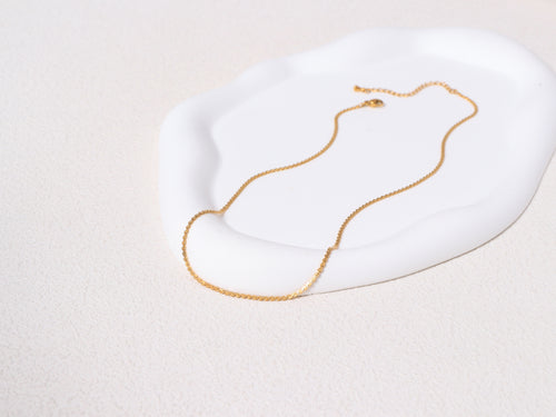 Allure Gold Chain resting on a neutral-toned jewelry base, showcasing the full length and minimalist 14k gold design.