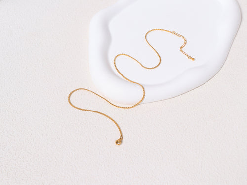 An opened Allure Gold Chain resting on a neutral-toned jewelry base, showcasing the full length and minimalist 14k gold design.