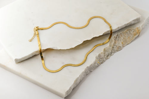 Cleo Necklace arranged in soft curves on a textured surface, capturing its flexible structure and elegant shine in 14k real gold.