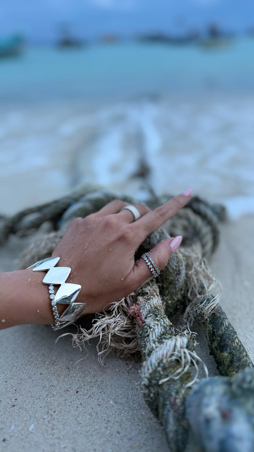 Hand with silver bracelet and ring on a rope on a beach