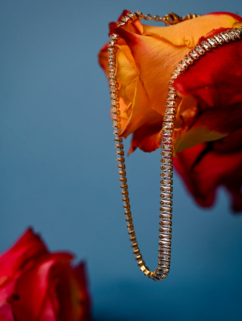 Close-up of the Lustre Necklace resting on flowers, highlighting its sparkling crystals and 18k gold-coated stainless steel links.